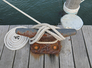 White docking line around a rusty cleat on a wooden pier.