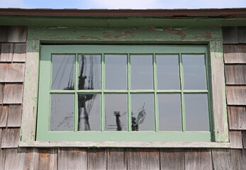 An old wooden crumbling green window in an old house reflects the masts of ships.