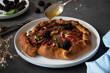 Figs galette. Hand pouring honey over traditional rustic fruit homemade pie, top view.