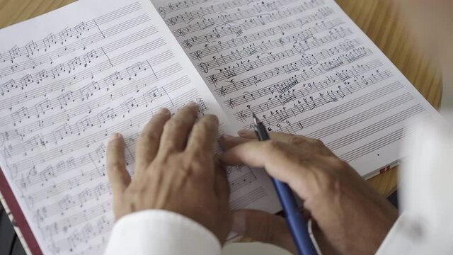Manos de m&uacute;sico escribiendo y leyendo partituras musicales 4K