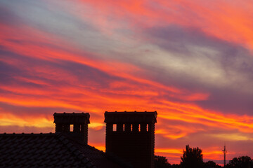 Fototapeta premium Golden sunset. Only the silhouettes of the houses are visible in orange sky. Orange evening sunset sky above house roof with small suburban houses at horizontal line.