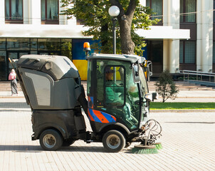 A car for cleaning garbage and fallen leaves is driving down the street. Autumn work in the sity.