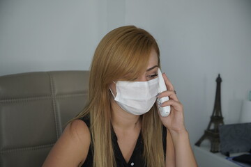 Portrait of blonde business woman in face mask talking on mobile phone, smartphone in female hand close up. Concept of communication during coronavirus pandemic