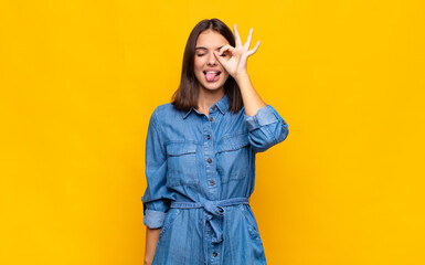 young pretty woman smiling happily with funny face, joking and looking through peephole, spying on...