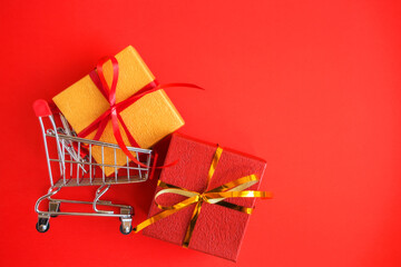 Shopping cart, small gifts boxs on a red background with a copy of the space. Christmas online shopping.