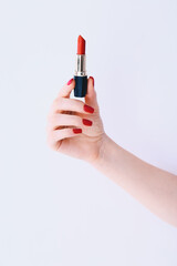 Woman hand with long red manicure on nails holding red lipstick on white background