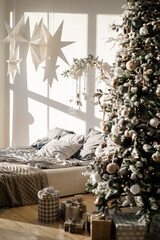Bedroom decorated by Christmas. Cozy Xmas home interior. New year decoration. bright room with Christmas tree in the bedroom. Gifts under the tree.