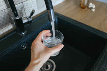 Human hand holding glass pouring fresh drink water at kitchen faucet