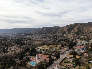 Fototapeta na wymiar Vista aérea panorámica desde un dron, de un pueblo en un valle, con una cordillera cubierta de vegetación y nubes grises.