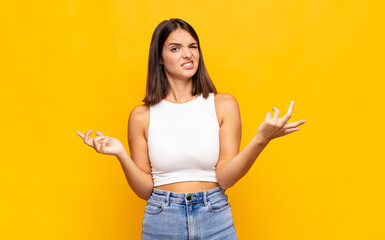 young pretty woman shrugging with a dumb, crazy, confused, puzzled expression, feeling annoyed and...