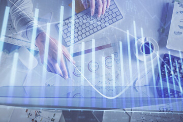 Multi exposure of man's hands typing over computer keyboard and forex graph hologram drawing. Top view. Financial markets concept.