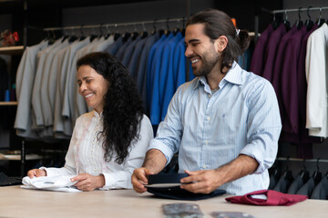 Cheerful brazilian coworkers folding shirts inside business store. owner, small business,...