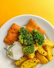 Fried fish, rice, brocolli and baked potato dish top view yeallow background