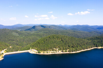 Beautiful lake, mountain peaks in light fog, aerial view from drone. Coniferous forests on banks of...