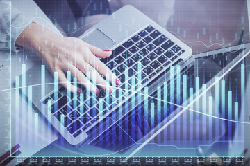 Double exposure of businesswoman hands typing on computer and financial graph hologram drawing. Stock market analysis concept.