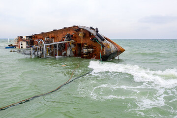 Naklejka premium Top view of sinking tanker shot by drone. Inverted tanker wrecked on Black Sea coast of Odessa. Empty tanker leaned to one side and ran aground by during storm with strong wind.
