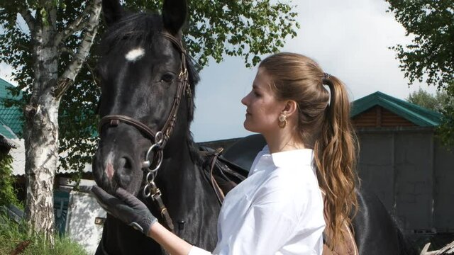 Girl in a white shirt and gloves stroking a horse