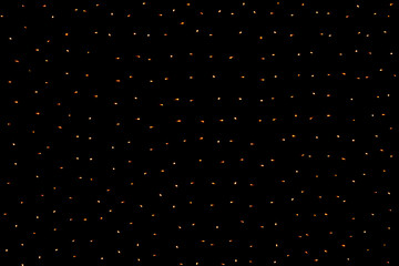Many small glowing orange lights from a garland on a black background. Burning light bulbs in the...