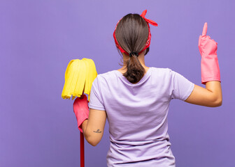 young pretty woman standing and pointing to object on copy space, rear view