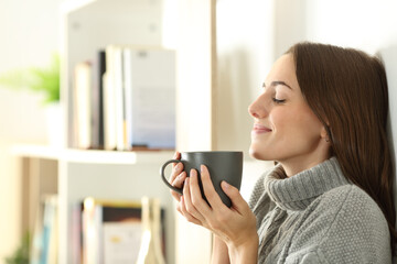 Satisfied woman smelling coffee in winter at home