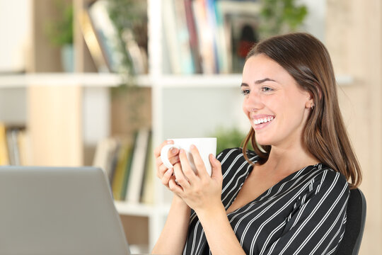 Happy woman drinking coffee looks away at home