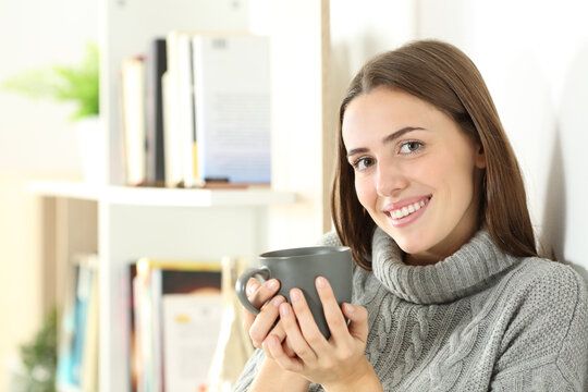 Happy woman looks at you holding coffee cup in winter