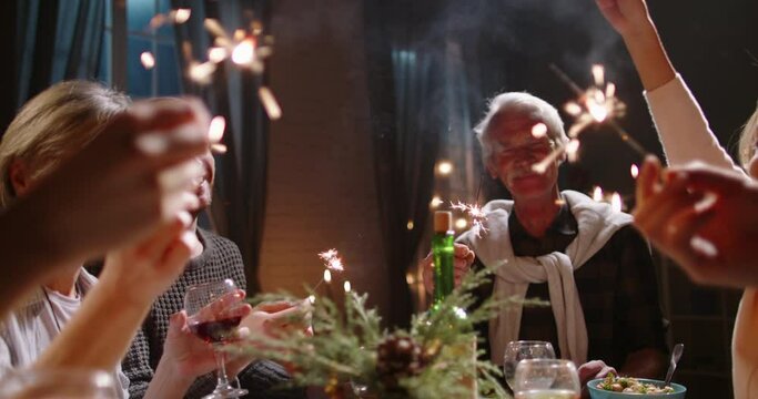 Large happy caucasian family celebrating christmas or new year together, holding sparklers at party dinner table and making wishes - celebration concept 4k footage