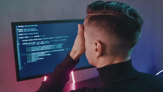 Back view of developer having stress in the office. Man programmer has a headache at office work. Overworking concept.