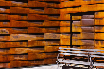 Close-up of brown metal tiled wall with empty bench. Rustic rectangular pieces creating pattern