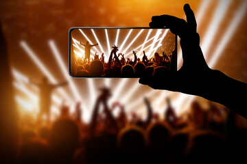 Silhouette of hand using camera phone to take pictures and videos at pop concert, festival