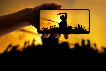 Silhouette of hand using camera phone to take pictures and videos at pop concert, festival
