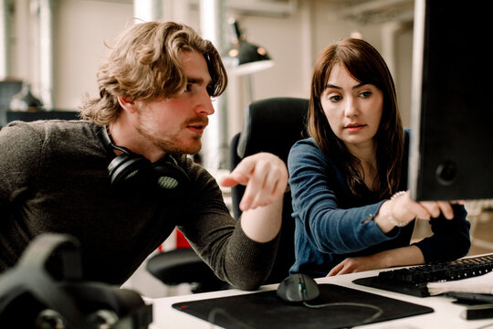 Female professional showing computer to coworker at workplace