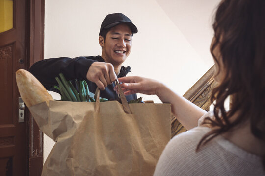 Smiling delivery man delivering vegetables to customer while talking at doorstep