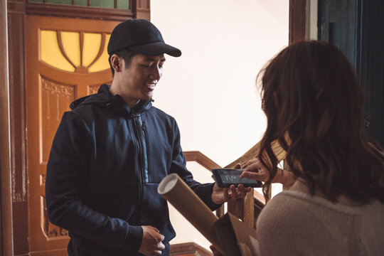 Customer signing on smart phone while delivery man standing at doorstep