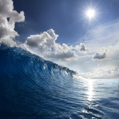 Blue Ocean Wave moving to a shore. Bright Day with sun and white puffy clouds on the sky