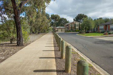 Fototapeta na wymiar Pedestrian walkway in a quiet residential neighbourhood with some suburban houses in the distance. Concrete footpath in an Australian suburb with Eucalyptus trees long the road. Copy space for text.
