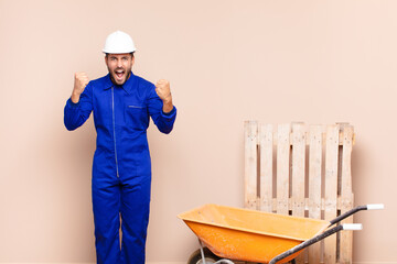 young man feeling happy, positive and successful, celebrating victory, achievements or good luck construction concept