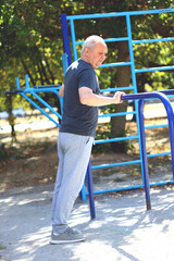 Obraz premium Senior man doing exercises in the outdoor gym. The concept of maintaining health at any age. Recovering from a heart attack or stroke. Selective focus. Toning.