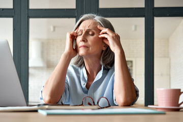 Tired stressed old mature business woman suffering from headache at work. Upset sick senior middle...
