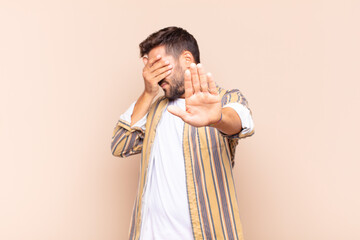 young man covering face with hand and putting other hand up front to stop camera, refusing photos...
