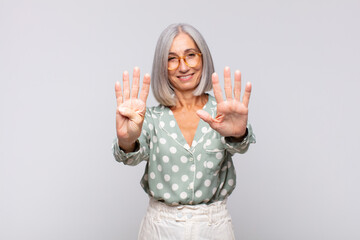gray haired woman smiling and looking friendly, showing number nine or ninth with hand forward,...