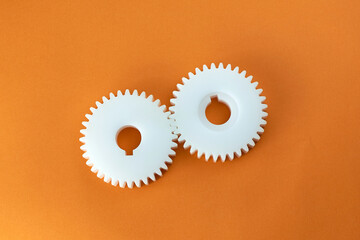 White plastic gears on an orange background, top view. Rust-proof