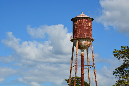 A rusty water tower with pealing paint and clouds in the background. 