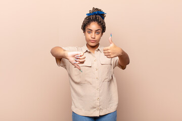 young afro woman feeling confused, clueless and unsure, weighting the good and bad in different...