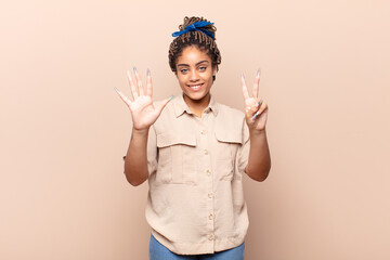 young afro woman smiling and looking friendly, showing number seven or seventh with hand forward,...