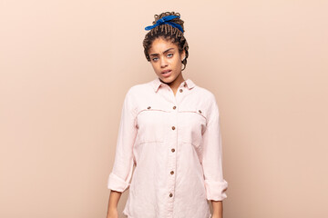 young afro woman feeling puzzled and confused, with a dumb, stunned expression looking at something...