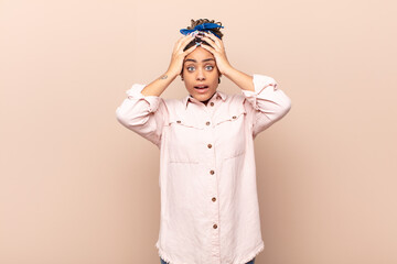 young afro woman feeling horrified and shocked, raising hands to head and panicking at a mistake