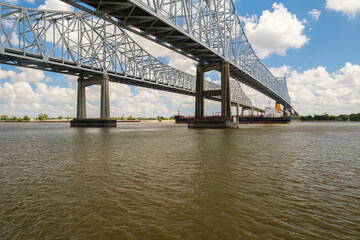 Interstate 10 Twin Span bridge over the Mississippi River in New Orleans, Louisiana with a cargo ship cruising by.