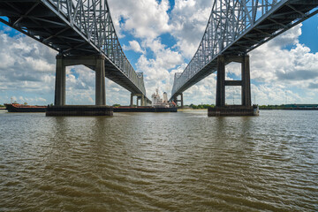 Interstate 10 Twin Span bridge over the Mississippi River in New Orleans, Louisiana with a cargo ship cruising by.