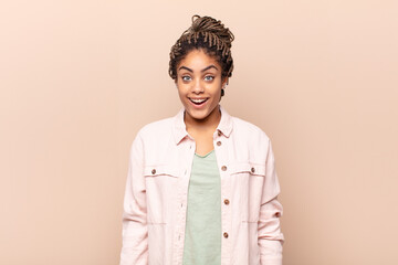 young afro woman looking happy and pleasantly surprised, excited with a fascinated and shocked...